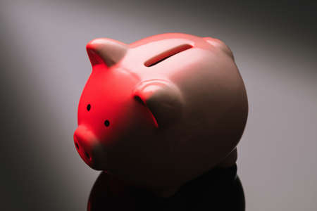 Ceramic piggy bank on a gradient background illuminated by red light, close-upの写真素材