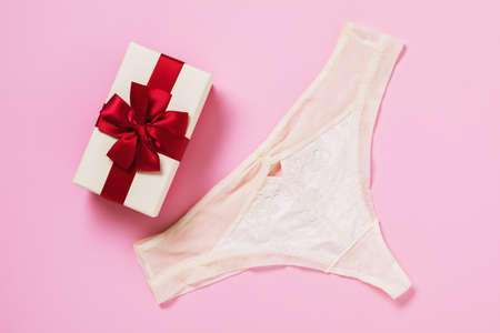 Light beige women's panties and a gift box with a bow on a pink background, top view.