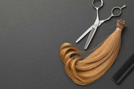 Scissors, a comb and a cut strand of blond female baby hair with copy space on a black background. Concept on the topic of hairdressing services.の写真素材