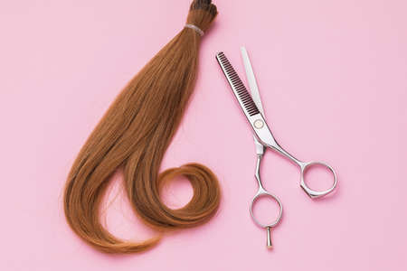 The cut off strand of female childrens hair of light brown color and scissors on a pink background, top view. Hairdressing servicesの写真素材