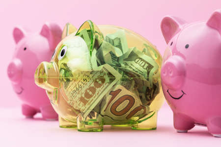 Three piggy banks on the table, one of them transparent, full of dollars.の写真素材