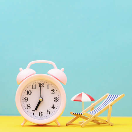 Alarm clock and toy deckchair with an umbrella from the sun on a colored background, concept of time...