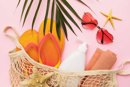 Beach accessories in a bag, sunglasses and a palm leaf on a pink background, summer background.