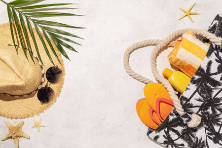 Beach accessories bag, hat, sunglasses and palm leaf on light background with copy space.