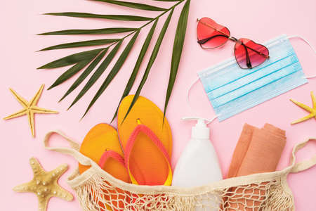 Chico leaf, sunglasses, beach slippers and medical mask on pink background.の写真素材
