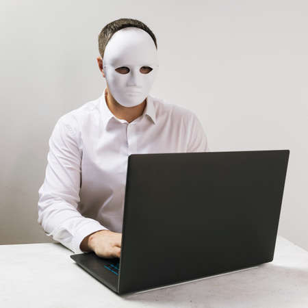 A man in a mask works behind a laptop, the concept of anonymity on the Internet.の写真素材