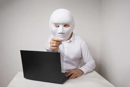 A man working at a laptop, covers his face with a mask, the concept of anonymity on the Internetの写真素材