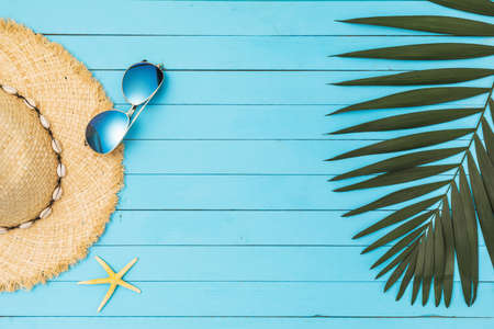 Hat, sunglasses, starfish and palm leaf on a wooden blue background with copy space in the centerの写真素材