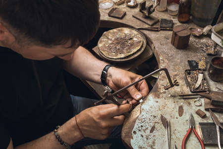 A jeweler saws a small piece of metal to repair a gold ring in his workshopの写真素材
