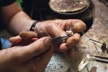 A jeweler disassembles a gold ring with pearls in a workshop, close-upの写真素材