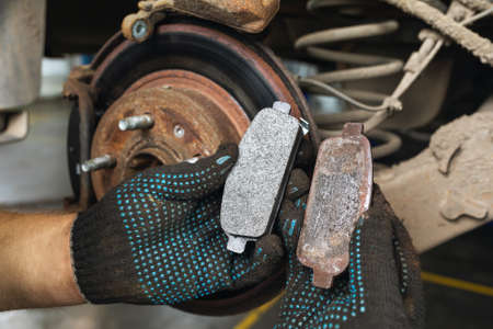 The car mechanic shows for comparison a worn brake shoe and a new one against the background of an automobile brake disc with signs of corrosionの写真素材