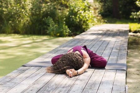 Woman balasana exercise sitting on a performing mat in the park on a sunny morning, child's pose