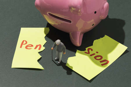 Elderly man with a crutch, an inverted piggy bank and a sheet of paper torn in half with text, concept on the topic of no savings in retirement age, a toy man made of plasticの写真素材