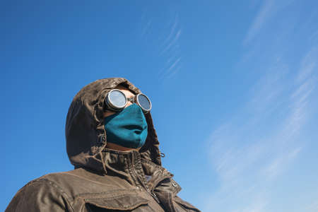 A man in a hood, in vintage steampunk goggy glasses and a protective mask against a blue skyの写真素材