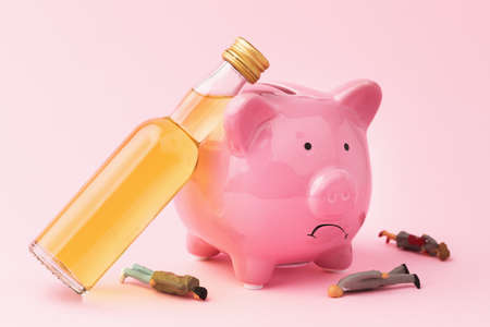 Whiskey bottle, piggy bank and plastic toy men on pink background, concept of alcoholism and drunkenness on last moneyの写真素材