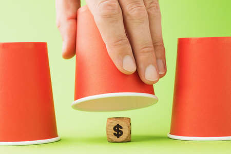 Raised glass and wooden cube with dollar symbol underneath, thimble gambling concept
