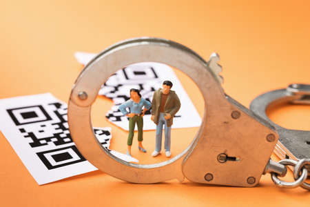 Plastic toy men, handcuffs and torn in half QR code on a colored background, the concept of...