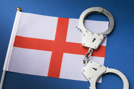 England Cross of St George Red White Flag and handcuffs on blue background, crime conceptの写真素材