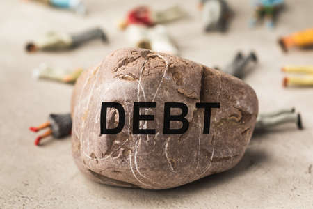 Stone with text and plastic toy men on the table, debt conceptの写真素材