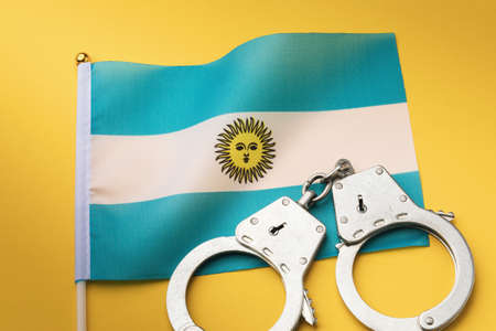 Argentina flag and handcuffs on a yellow background, a concept on the theme of crime in the country, top viewの写真素材