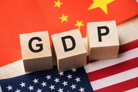 Wooden cubes with the text on the background of the flags of China and America, the concept on the topic of comparing the GDP of the USA and Chinaの写真素材