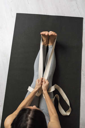 A woman performs an exercise with straps to stretch the muscles of the back, sits on a mat in the studio, top viewの写真素材