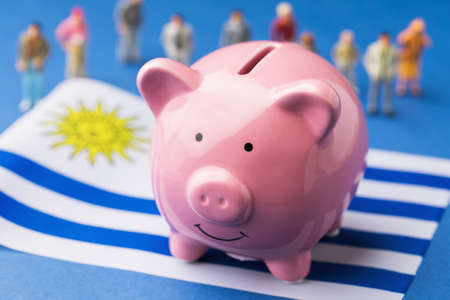 Piggy bank, Uruguayan flag and plastic toy men on a colored background, concept on the theme of income of the population of Uruguayの写真素材