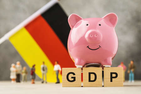 Piggy bank, wooden cubes with text, toy men made of plastic and a flag on an abstract background, a concept on the theme of Germany GDPの写真素材