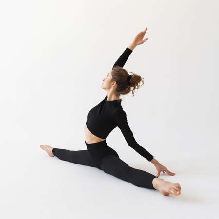A young woman is engaged in stretching the muscles of the legs, performs a transverse split on a...