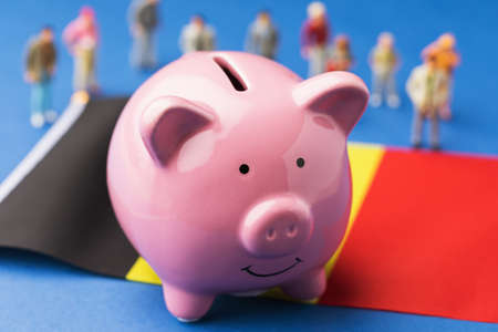 Piggy bank, flag and plastic toy people on a colored background, a concept on the income of the Belgian populationの写真素材