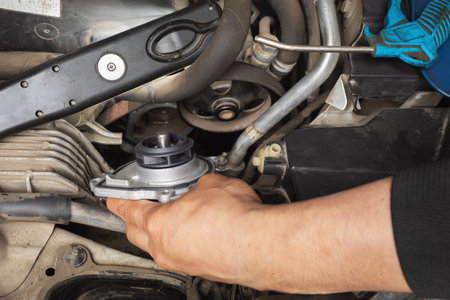 Auto mechanic installing a new engine cooling pump in a car at a service station