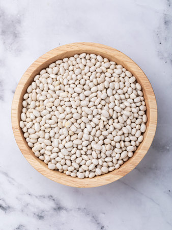 White beans in a wooden bowl on the table, top view