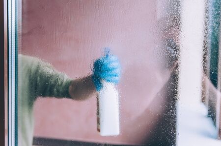 Man in gloves washes a window with a spray bottle.