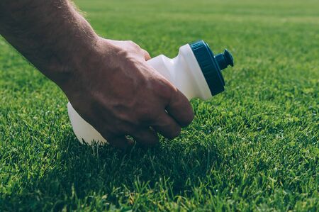 The athlete takes a sports water bottle on the green lawn of the stadiumの写真素材