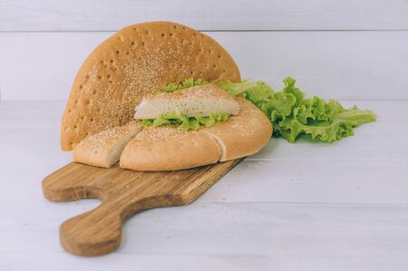 Loaf of bread with greens sliced on a cutting board on a white tableの写真素材