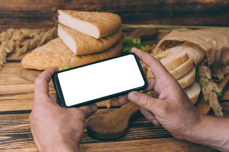 Mock up smartphone in hand on background with fresh bread on a wooden backgroundの写真素材