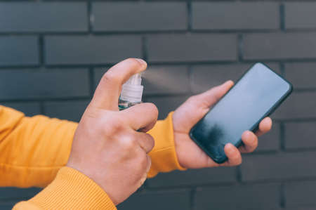 A man disinfects a smartphone in his hand. Means for protection against the COVID-19の写真素材