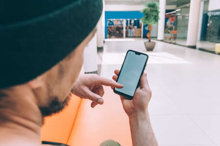 Mock-up technology. Man holds a smartphone in his hands against the background of a shopping centerの写真素材