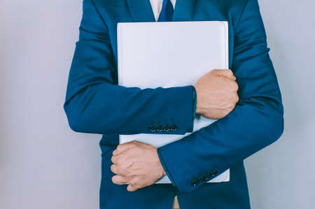 Businessman with a blue jacket on a gray background with a laptop in his handsの写真素材