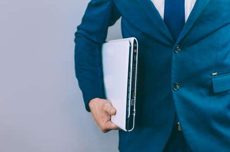 Businessman with a blue jacket on a gray background with a laptop in his handsの写真素材