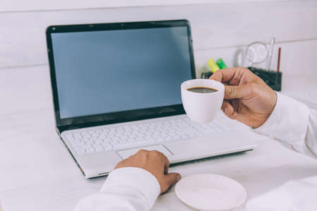 Mock-up Technology. Businessman holds a smartphone in his hands, on a background of laptop and coffee on a wooden tableの写真素材