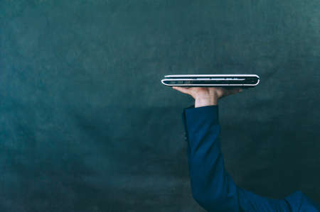 Businessman with jacket on a dark background with a laptop in his handsの写真素材