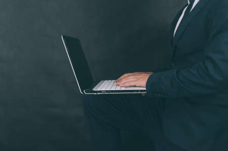 Businessman with jacket on a dark background with a laptop in his handsの写真素材