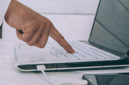 Businessman works on a laptop and charges a smartphone on a white, wooden table