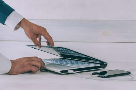 Businessman works on a laptop and charges a smartphone on a white, wooden table