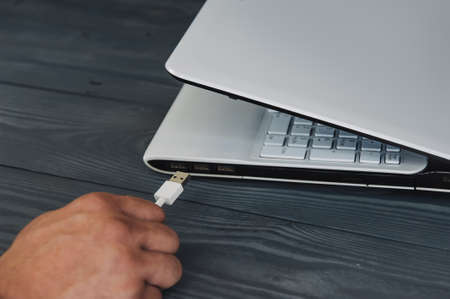 Man hold cable to white laptop on wooden backgroundの写真素材