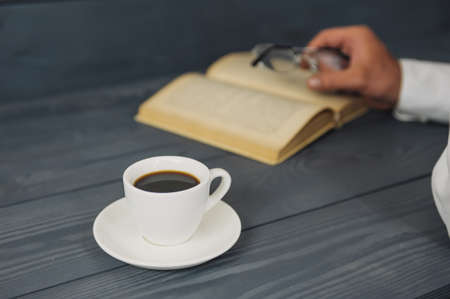 Concept on the topic of education. A man with glasses reads books, on a wooden background with coffeeの写真素材