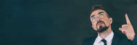 Businessman in a jacket with a shirt and tie, on a dark background with glasses shows a finger to the topの写真素材