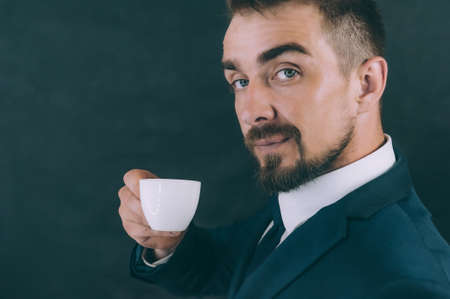 Businessman with jacket on a dark background with a coffee in his handsの写真素材