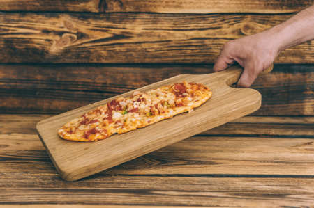 The guy holds pizza on a wooden table. Fast food cooked at homeの写真素材